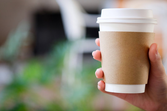 Hand holding paper cup of hot coffee in cafe.