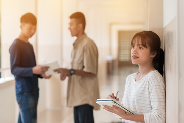 Obraz premium Education learning Concept: Confident Asian Students Cute girl taking note with smiling at Outside classroom in university with blur young mens her friends background