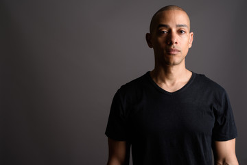 Handsome bald man wearing black shirt against gray background