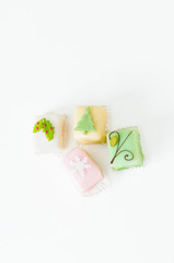 White, light pink, yellow and green petit fours, small cake squares decorated with fondant, chocolate, sugar icing and marzipan Christmas ornaments