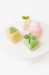 White, light pink, yellow and green petits fours, small cake squares decorated with fondant, chocolate, sugar icing and marzipan Christmas ornaments