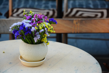 Decorative composition of multicolored wildflowers in vase on the table of street cafe.