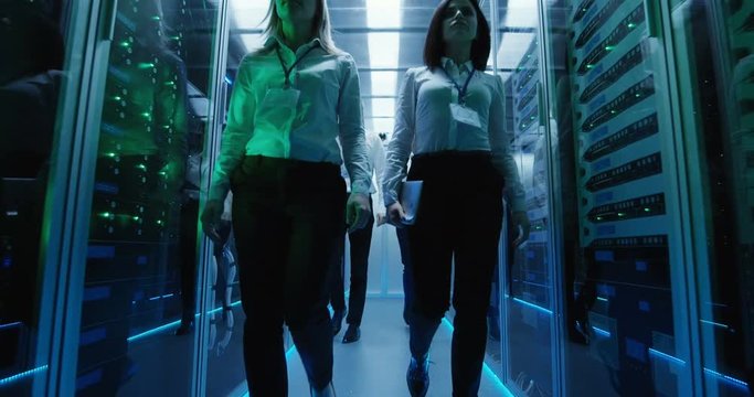 Wide shot of workers in a data center walking between rows of server racks on their way to a meeting
