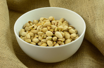 Roasted pistachio nuts in white snack party bowl on burlap © merrimonc