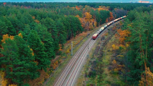Aerial view of the freight train moves through the autumn forest. Back view