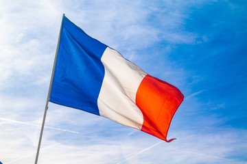 French flag waving on the pole on a blue sky with clouds during a summer in Paris, France. The flag of France contains the colours blue, white and red