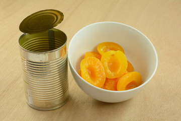 Canned apricot halves in white bowl next to opened can on wooden table