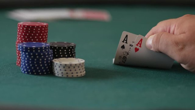 Close-up of gamblers hands beside a stack of casino chips as he checks his poker cards and sees he has pocket aces