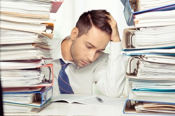 Tired young businessman with stack of papers and laptop