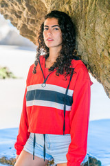 Portrait of latino woman with curly hair, red top and denim shorts at beach