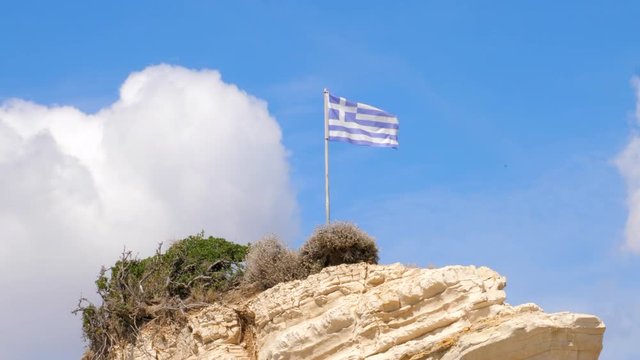 Greek flag waving in the wind on a cliff with a big coud