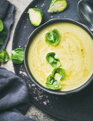 Seasonal brussels sprouts vegetable cream soup in black bowl and fresh green brussel sprouts over black plate, top view, close-up. Vegan, vegetarian, healthy, dieting food concept
