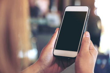 Mockup image of a woman holding white mobile phone with blank black desktop screen with blur background