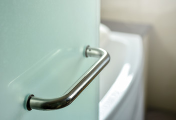 Glass door handle of a glass partition shower unit. Bathroom glass door detail with bath tub in the...