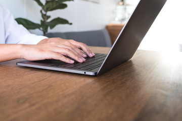 Closeup image of woman's hands using and typing on laptop keyboard on wooden table in office