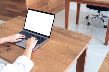 Mockup image of a woman using and typing at laptop with blank white desktop screen on wooden table in office