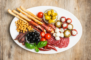 Various snacks of cold meat, cheese, bacon, grissini bread sticks, olives are served on a white...
