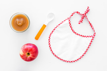 Baby food concept. Apple puree in bowl near bib, apple, spoon on white background top view