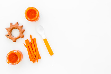 Healthy food for small babies. Carrot puree in bowl near carrot slices, spoon, toy on white background top view space for text