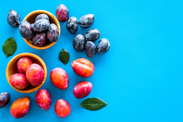 Plums on dinning table. Fresh raw red and blue plum in wooden bowl on blue background top view copy space