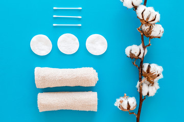 Products made of cotton. Bath accessories. Towels, cotton pads and swabs near dry cotton flowers on blue background top view pattern