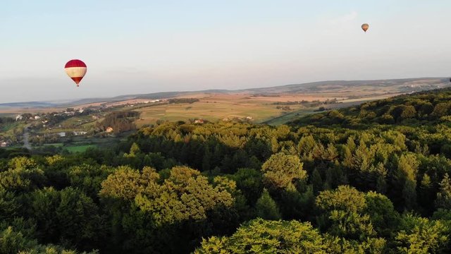 Aerial view of hot air balloons flying over the green woods. Nature beauty, impressive landscape