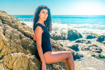 Portrait of latino woman with curly hair, black swimsuit at beach