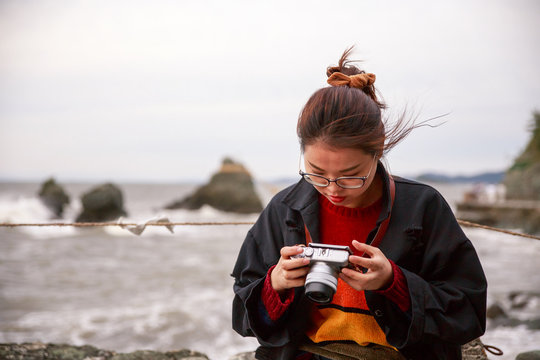 Young woman checks photos on back of camera at Wedded Rocks in Ise, Japan
