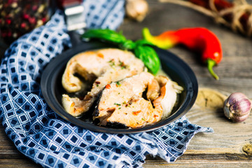 stewed salmon with spices and spicy sauce in a frying pan on a wooden table