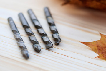 metal drill closeup on wooden background. close-up. there are maple leaves, no focus