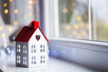 Toy house with hole in form of heart near window in daylight with garland lights on background. - 229865846