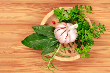 An overhead photo of garlic, aromatic kitchen herbs and spices, shot from above in a wooden bowl on a rustic wooden background with copy space