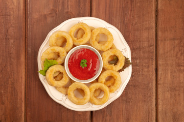 A photo of squid rings with a tomato sauce, shot from the top on a dark rustic wooden background with a place for text