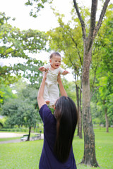 Fototapeta premium Asian mother throws up happy infant baby boy in arms at garden.