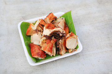 Grilled chicken with chopped on banana leaf in a tray against cement table with copy space.
