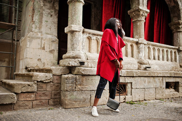 Stylish african american woman in red coat posed against old columns.