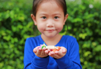 Asian child girl holding some thai sugar and fruit toffee with colorful paper wrapped in her hands. Focus at candy in her hands.