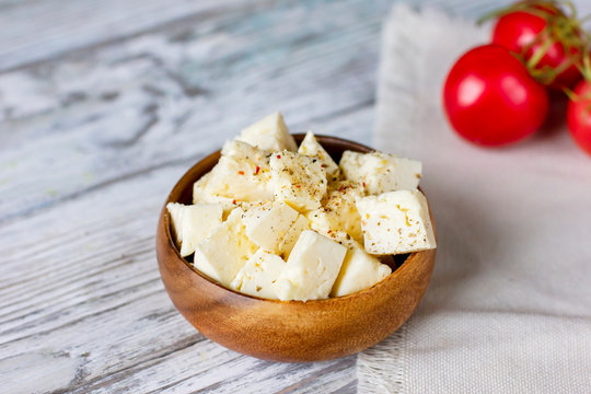 Feta cheese cubes in wooden plate on white wood