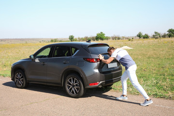 Man pushing broken car along country road