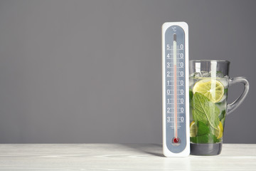 Thermometer and cup of mojito on wooden table against grey background. Space for text