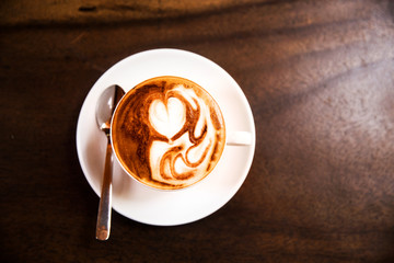 Cup of hot cappucino is standing on the wooden table.