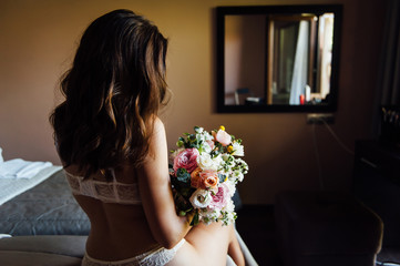 Sexy beautiful nude brunette bride with bouquet and wavy hair style in white erotic underwear.