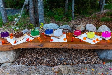 Various colors of silk lantern boats mounted on cedar wood and surrounded by orange flowers on a wooden bench - 4/5 - Wide angle picture taken outside in northern Quebec
