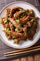 Asian food: Teriyaki beef with green onions and sesame close-up on a plate. Vertical top view