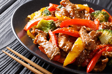 Freshly prepared Asian spicy teriyaki beef with red and yellow bell peppers, broccoli and sesame seeds close-up on a plate. horizontal