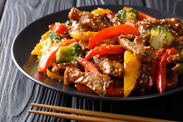 delicious Asian teriyaki beef with red and yellow bell peppers, broccoli and sesame seeds close-up...