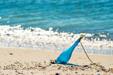 Fototapeta na wymiar Blue bottle with a message, lying on the seashore