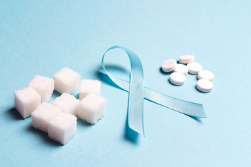 Blue ribbon with refined sugar and pills on a blue background. World diabetes day concept.