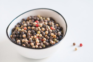 Different mixed pepper seeds in a white bowl on a white background. Macro photography.