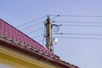 Electric pole and red tile roof on blue sky background. Power supply in countryside.